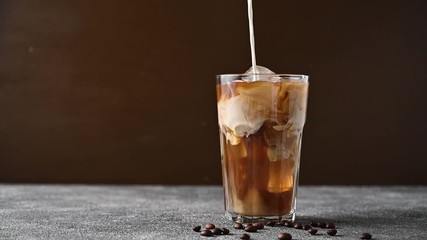 Add cream to iced coffee. Slow motion milk pouring into a glass cup with coffee and ice. - Powered by Adobe