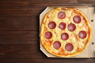 Tasty pepperoni pizza in cardboard box on wooden table, top view. Space for text