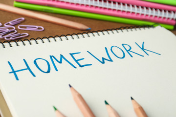 Word HOMEWORK written in notebook on wooden table, closeup