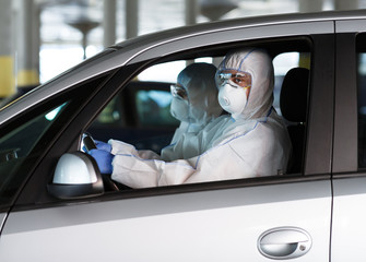 People in coronavirus protective suits driving a car