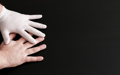 Two hands on a black background. One hand in a medical glove.