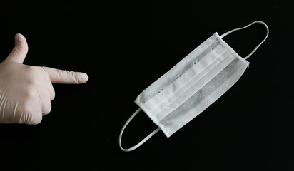 Hand in latex glove points medical mask on black background