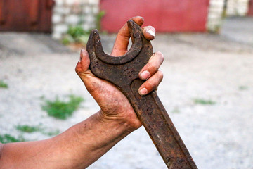Fototapeta premium big old rusty wrench is held by male dirty calloused hands.