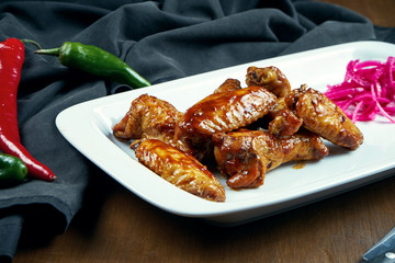 Great beer snack - spicy baked buffalo wings. BBQ wings with garnish of salad on white plate. Close up. Pub food
