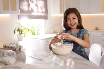 Obraz na płótnie Canvas Cute little girl cooking dough in kitchen at home