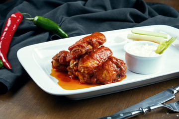 Great beer snack - spicy baked buffalo wings. BBQ wings with garnish of salad on white plate. Close up. Pub food