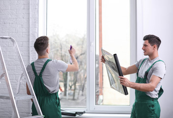 Professional workers tinting window with foil indoors