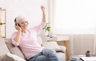 Joyful senior lady enjoying music in new headset at home