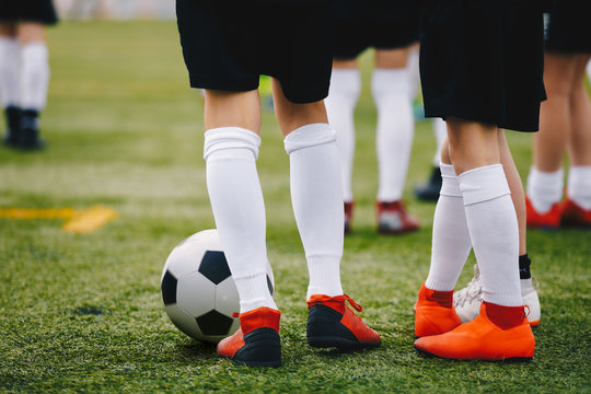 Soccer players with ball on a training field. Young junior level athletes in football cleats and uniforms on grass training ground. Closeup image of soccer players legs. Football background