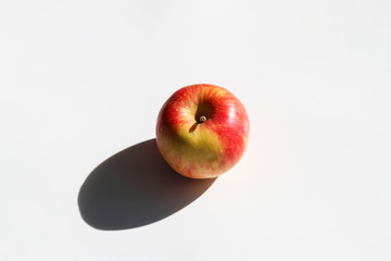 Fresh apple with strong shadow on white background at sunny day. Trendy minimal food concept. Organic natural fruit