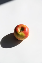 Fresh apple with strong shadow on white background at sunny day. Trendy minimal food concept. Organic natural fruit