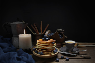 Obraz na płótnie Canvas national dish pancakes, pancakes, pita with blueberries, linen napkin, a candle burns, a cup of tea, an old mocha coffee machine, a concept of traditional cuisine