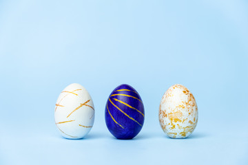Three easter trendy colored classic blue and golden decorated eggs on blue background. Happy Easter card with copy space for text. Minimal easter style.