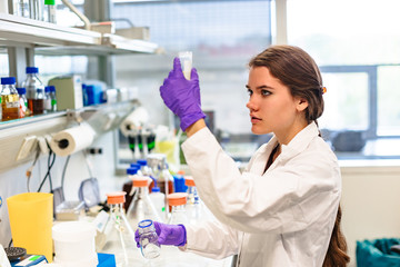 Girl laboratory assistant examines liquid in flask