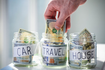 Male hand puts 100 dollars in a glass jar with the inscription travel.