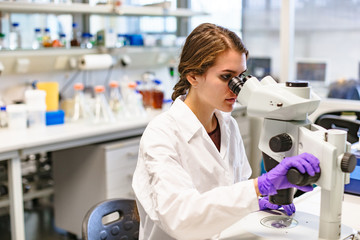 Scientists woman looking through microscope in lab