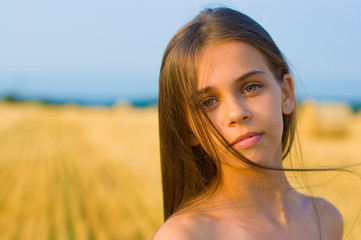 horizontal close-up portrait of a long-haired teenager girl on a background of sky and a beveled wheat field