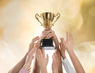 People with gold trophy cup on color background, closeup
