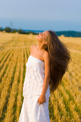 vertical photo of a long-haired teenager girl against a blue sky and a golden wheat field