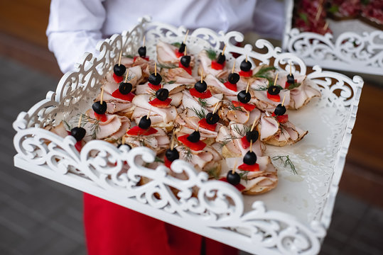 Cropped images of waiter holds cold snacks on wooden stand with cold meats. Variety of tasty delicious snacks. Corporate birthday party event