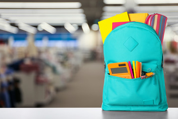 Bright backpack with school stationery on table in shopping mall. Space for text