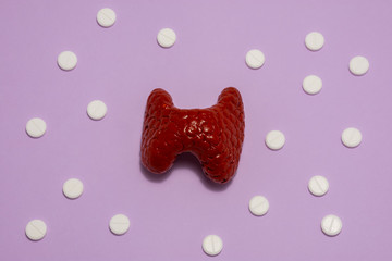 Model or figure of thyroid gland, which corresponds to anatomical original, is located in purple background surrounded by white pills ornamented in polka dots. Photo for use in endocrinology, hormones