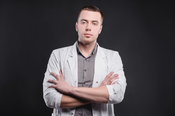 Young, pretty man in a medical coat on a gray background. The concept of medical education and medical activity