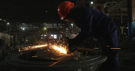 Working in a mask and headphones cleans joints angle grinder on metal parts blanks