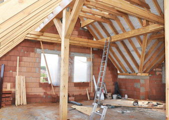 Incomplete attic with roof trusses, wooden roof beams, braces and windows inside. Converting an attic into a room.