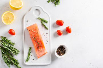 Fresh raw salmon red fish fillet with spieces, herbs, lemon and tomatoes on white background, side...