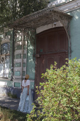 Look of russian girl in beautiful retro dress, vintage hat and porch door of old house in Astrakhan...