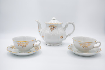Vintage white teapot with tea cups  with golden rim in classic style isolated on white background