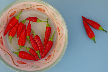 Composition of spicy red chillies in a bowl with water, you can see some resting on a blue paper...