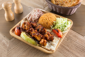 Delicious Grilled Chicken Wings Kebab with bulgur pilaf, onion and salad on rustic black wooden table background. Dark photography concept.