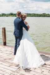 bride and groom are in an embrace on the pier in the background of lake