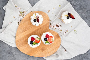 Top view of vegan cupcakes with berries and coconut cream on a wooden board.