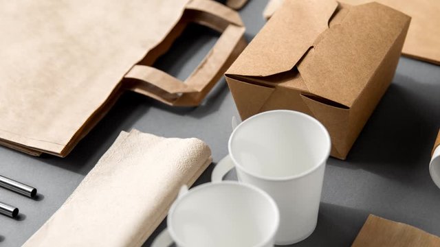package, recycling and eating concept - disposable paper container for takeaway food with cups, bags, napkins and cutlery on table