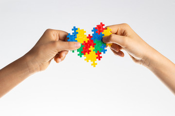 World autism awareness day concept. Children hands holding colorful puzzle heart on white background - obrazy, fototapety, plakaty