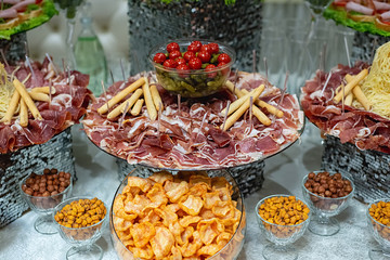 Banquet table with cheese, сhips, nuts, cold meats, sliced sausages, cucumbers, tomatoes. Variety of tasty delicious snacks. Food concept