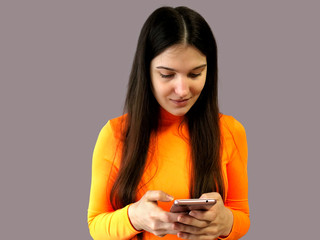 Young beautiful girl with dark hair in a bright orange sweater on a gray background. With phone in hand