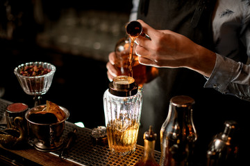 Close-up bartender using beaker professionally pours drink into glass shaker