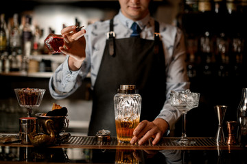 young barman adds ingredient for cocktail to glass shaker.