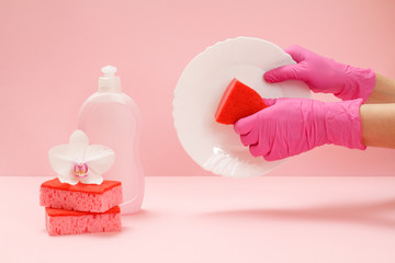 Women's hands in latex gloves with a sponge and a plate on the pink background.
