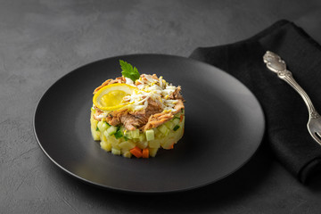 Salad with canned tuna and vegetables in culinary ring on black plate. Dark background. Beautiful serving in the restaurant.