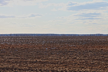 Endless brown ploughed field against a blue sky on a spring day &mdash; soil cultivation, agriculture, rural landscape