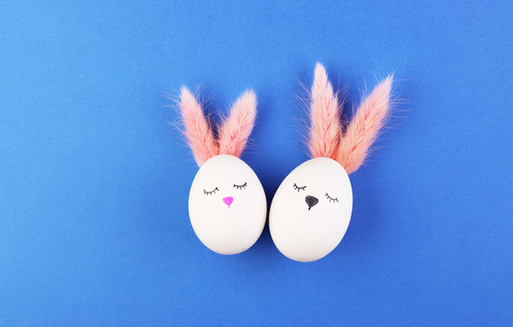 white Easter eggs in the form of bunnies with cute faces and fluffy ears. eggs on a blue background for Easter