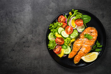 Grilled salmon fish steak with vegetables on black.