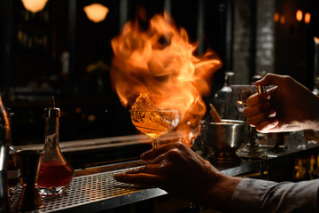 Professional barman carefully spray to splashing cold alcoholic drink and burn it.
