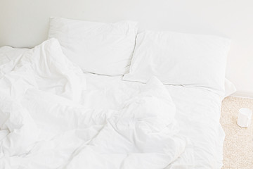 Cozy white bed in the morning. White sheets and pillow on bed in modern white room. Lazy days. Stay home. Comfortable place. Relax on weekend in hotel room. Messy bed
