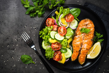 Grilled salmon fish steak with vegetables on black.